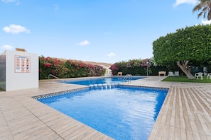 Una piscina con bordo piastrellato, circondata da vegetazione e un muro bianco con segnaletica di sicurezza.