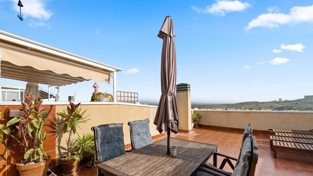 Eine Terrasse mit Tisch und Stühlen, Blumentöpfen und Blick auf die Landschaft.