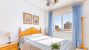 Une chambre à coucher avec un lit en bois, deux tableaux accrochés au mur, une fenêtre avec des rideaux, une table de chevet avec une lampe et un lampadaire.