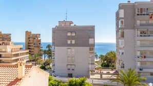 Un immeuble à plusieurs étages doté de balcons, offrant une vue dégagée sur la mer, et une clôture blanche en premier plan.