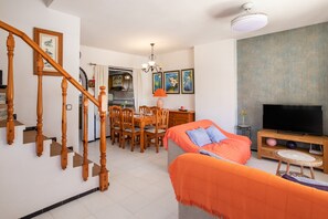 A living room with a sofa, TV, dining table, chairs, and a staircase.