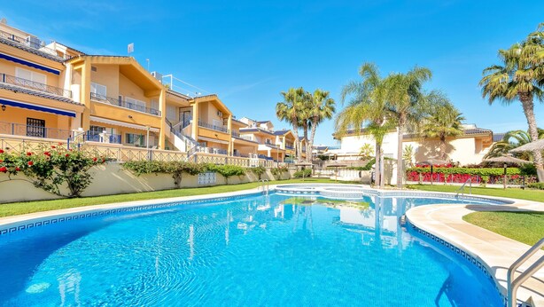 A swimming pool with a clear blue water surface, surrounded by a poolside area with a low wall and a few palm trees.