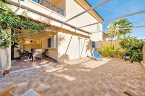Une terrasse couverte avec un sol carrelé, des meubles d’extérieur et une pergola ornée de plantes grimpantes.