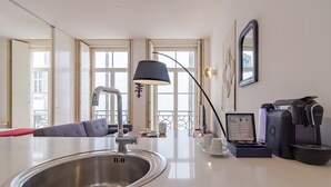 A modern kitchen with a stainless steel sink, a black pendant lamp, a coffee machine, and a seating area with a sofa and a dining table. - Twin Studio with Balcony view Clérigos Tower (Oporto)