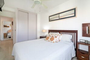 Une chambre à coucher comprenant un lit, une table de chevet, une lampe de chevet, un ventilateur de plafond, une armoire et un tableau encadré accroché au mur.