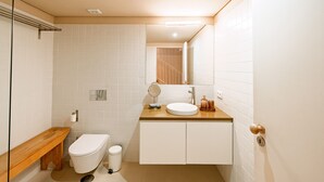 Een moderne badkamer met toilet, wastafel, spiegel en een houten bankje.