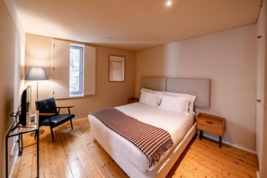 A bedroom with a bed, a desk, a chair, a lamp, and a window.