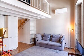 A modern living room with a grey sofa, a staircase, and a white railing. - Spacious Duplex Studio for 4 w/ balcony in Center (Oporto)