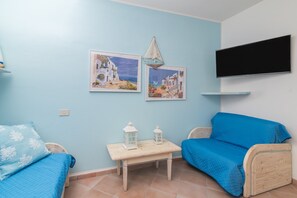 A room with a bed, a blue sofa, a small table with two lanterns, and two wall-mounted pictures.