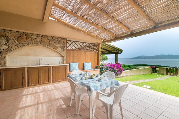 An outdoor kitchen with a stone wall, wooden cabinets, and a table with chairs.