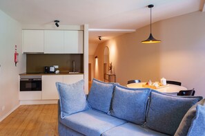 A modern kitchen with white cabinets, a built-in oven, and a dining area with a round table and blue chairs. - Typical One-Bedroom Apart for 3 in Center (Oporto)