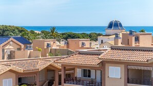 Una zona residencial costera con edificios de tejados de teja, una estructura en forma de cúpula y una playa al fondo.