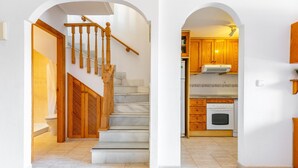 Una escalera que lleva a un baño, una cocina con armarios de madera y una pared blanca.