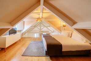 Een zolderkamer met een bed, een televisie op een kast, en een trap naar de bovenverdieping.