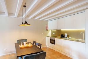 A modern kitchen with white cabinets, a wooden dining table, and a hanging pendant light.