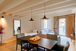 A modern room with a wooden dining table, two pendant lights, a sofa, a bed, and a large window.