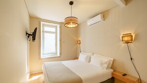 A bedroom with a bed, bedside table, lamp, window, and wall-mounted air conditioning unit. - Top Floor One Bedroom Apart for 3 nice Views (Oporto)