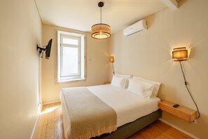 Ein Schlafzimmer mit Bett, Nachttisch, Lampe und Fenster.