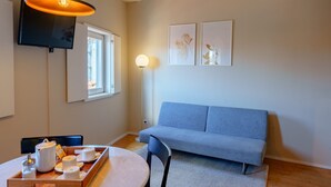 A modern living room with a sofa, a dining table with a tray of breakfast items, a flat-screen TV mounted on the wall, and a floor lamp. - Top Floor One Bedroom Apart for 3 nice Views (Oporto)