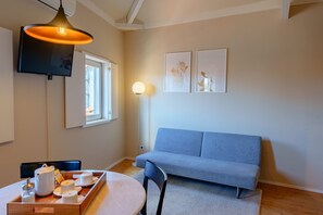 Ein modernes Wohnzimmer mit einer Couch, einem Esstisch mit Frühstücksangebot, einem Flachbildfernseher und einer Stehlampe.