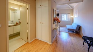 A room with a wooden floor, a white wardrobe, a small table with a vase, a grey sofa, and a black bench. - Top Floor One Bedroom Apart for 3 nice Views (Oporto)