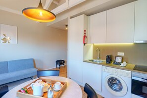 Ett kompakt bostadsutrymme med en soffa, ett matbord med ett bricka fyllt med diverse föremål, en tvättmaskin och ett köksområde med en diskho och en arbetsbänk.