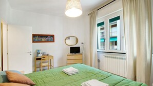 A hotel room with a green bed, a desk with a computer, a window with curtains, and a radiator. - Apartment "Sunrise" close to the Sea with Wi-Fi (Santa Margherita Ligure)