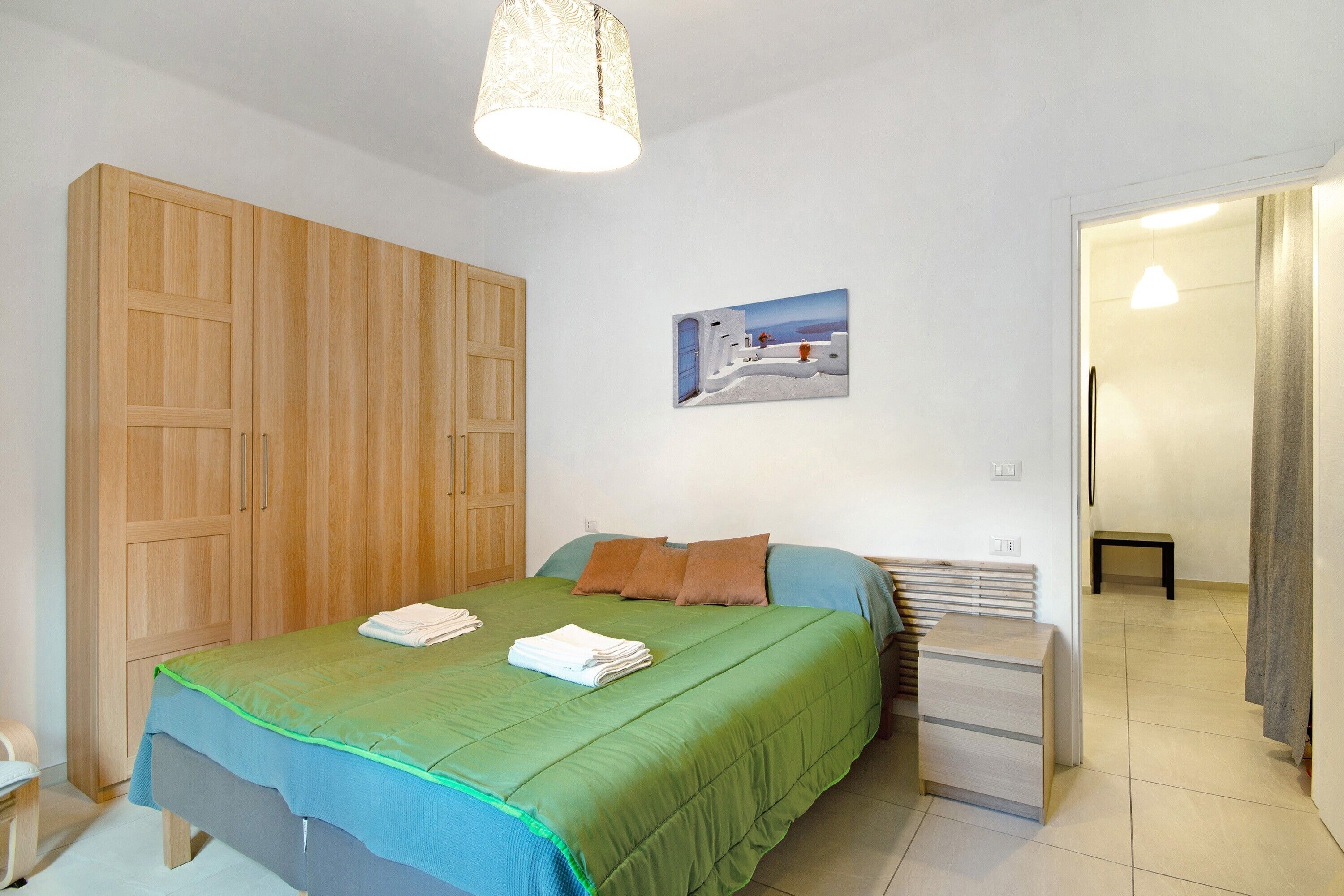 Een slaapkamer met een bed, een houten garderobe, een schilderij en een nachtkastje.