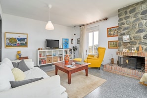 A living room with a sofa, a coffee table, a television, a bookshelf, a yellow armchair, and a fireplace.