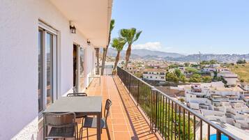 A balcony with a table and chairs, overlooking a residential area with houses and a mountain in the distance.