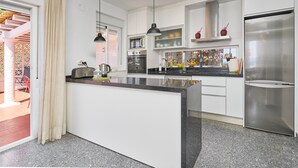 A modern kitchen with white cabinetry, a central island, stainless steel appliances, pendant lighting, and a view to an outdoor patio. - Villa "Casa Beto" with Sea View, Pool, Garden & Wi-Fi (Almuñecar)