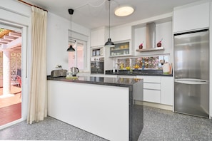 A modern kitchen with white cabinetry, a central island, stainless steel appliances, pendant lighting, and a view to an outdoor patio.