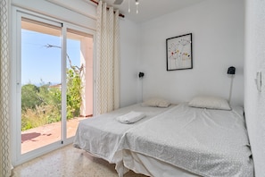 A bedroom with two beds, a sliding glass door to a balcony, a wall-mounted picture, and a ceiling light.