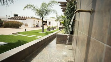 Uma trilha com um elemento aquático, uma palmeira e um edifício com fachada em azulejos.