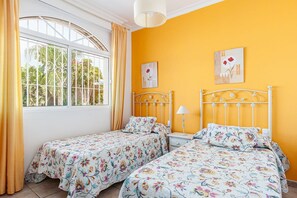 A room with two beds, a window with curtains, and two wall-mounted paintings.