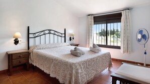 Ein Schlafzimmer mit einem Bett, zwei Nachttischen, einem Fenster mit Vorhängen und einem Wandventilator.