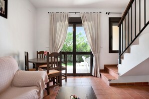 A room with a sofa, dining table, chairs, and a staircase.