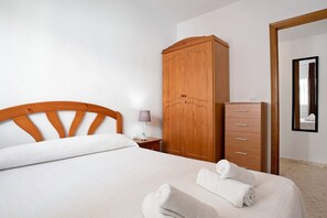 A hotel room with a bed, wooden wardrobe, a nightstand with a lamp, and a mirror on the wall.