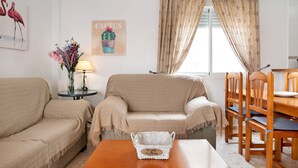 A living room with a sofa, a small table with a lamp, a cactus decoration, and a window with curtains.