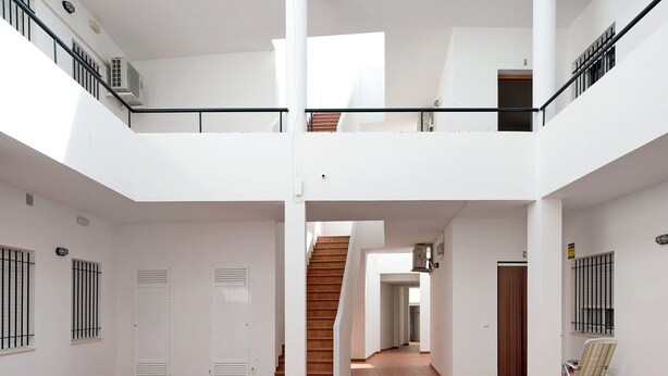 A spacious interior with a central staircase, white walls, and a tiled floor.