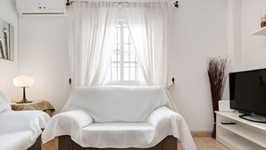 Et værelse med sofa, fjernsyn, lampe og et vindue med gardiner.