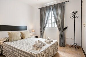 A hotel room with a bed, a nightstand, a lamp, a coat rack, and a window with curtains.