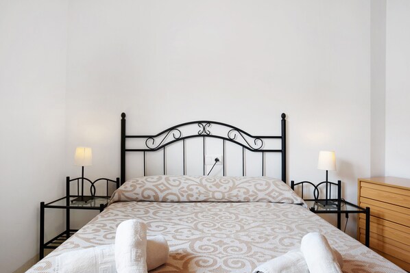 A bed with a patterned bedspread, two bedside tables with lamps, and a wooden dresser.