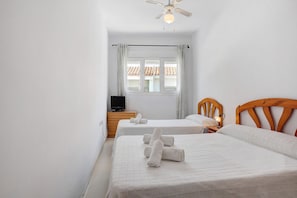 Een hotelkamer met twee bedden, een televisie op een houten dressoir en een raam met gordijnen.