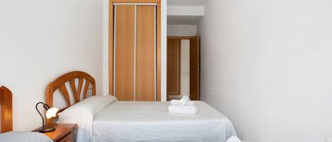 A hotel room with two beds, a wooden wardrobe, a nightstand with a lamp, and a bathroom door.