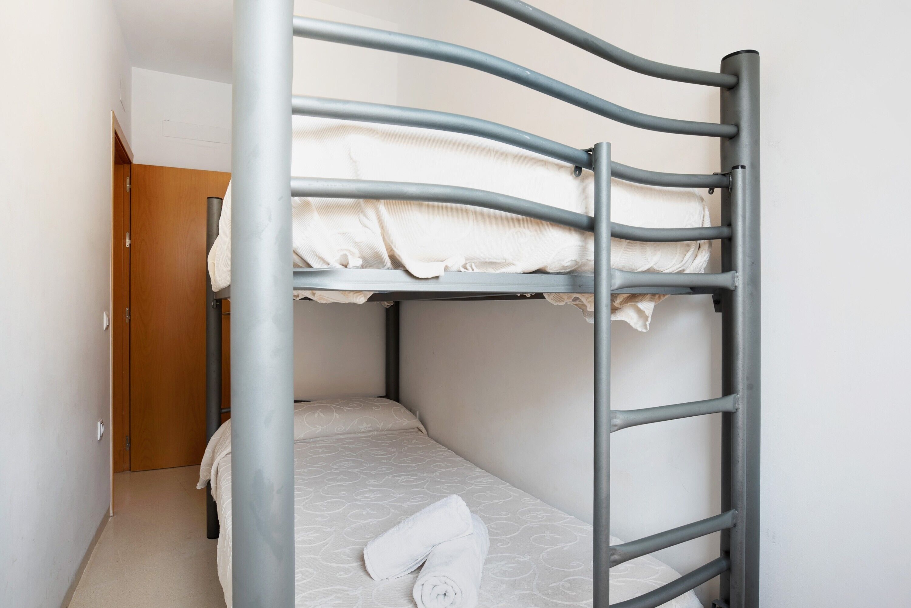 A bunk bed with a metal frame, a wooden door in the background, and a white towel on the lower bunk.