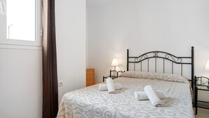 A neatly made bed with a patterned bedspread, a bedside lamp, and a wooden nightstand. - Holiday Home "Almadraba 2 - Andalmar" close to the Sea with Wi-Fi (Conil)