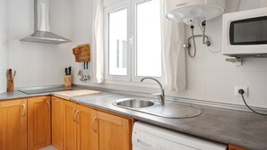 A kitchen with wooden cabinets, a stainless steel sink, a microwave, and a window with curtains. - Holiday Home "Almadraba 2 - Andalmar" close to the Sea with Wi-Fi (Conil)