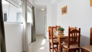 A dining area with a wooden table and chairs, a window with curtains, and a picture on the wall. - Holiday Home "Almadraba 2 - Andalmar" close to the Sea with Wi-Fi (Conil)