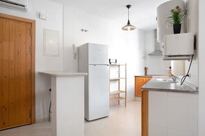 A modern kitchen with white cabinetry, a built-in refrigerator, a wooden door, and a hanging plant.